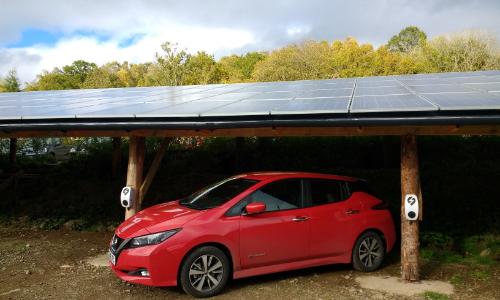 Photo of an electric car parked underneath solar panels