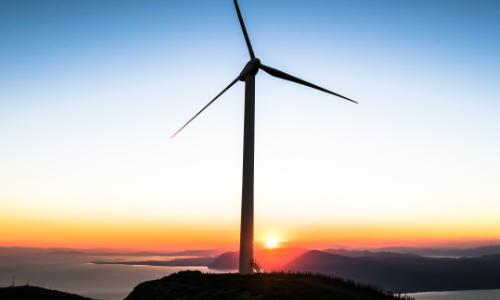 Photo of a wind turbine on an island with a sunset behind